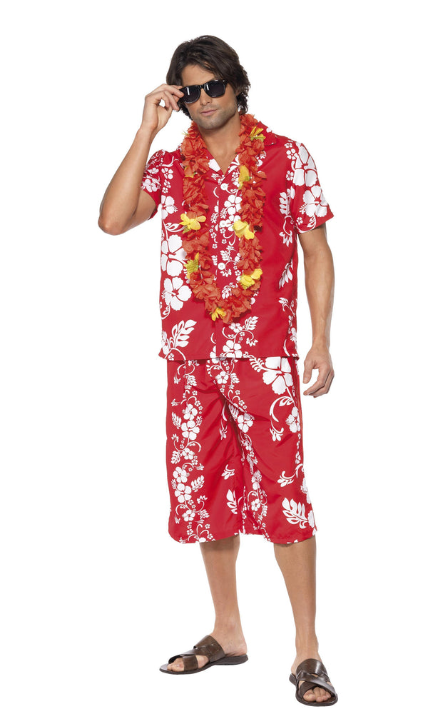 A man wearing a red Hawaiian costume with a lei, consisting of a short-sleeved shirt and matching shorts, standing against a white background.